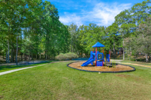 Exterior Playground, picnic table nearby, blue playscape, soft landing ground, slide, meticulously groomed grounds, lush foliage in background.