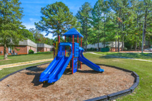 Exterior Playground, Blue Playscape, soft landing gorund, 3 slides, lush foliage in background, well groomed grounds, photo taken on a sunny day.