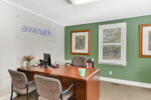 Interior Leasing office, green wall, avanath signage, window next to desk, desk with 3 seats, filing cabinet, new carpeting.