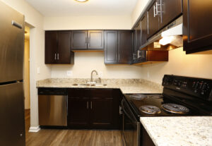 Interior Unit Kitchen, stone countertops, black and stainless steel appliances, dark brown cabinetry, dual sink, wood floors.