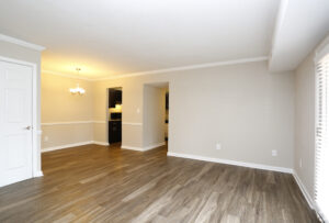 Interior Living Room, chandelier in dining area, wood floors, dark brown cabinets in kitchen area, neutral toned walls.